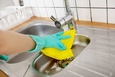 Cropped hand wearing protective glove while cleaning kitchen sink