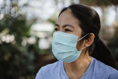 Close-up of woman looking away while wearing mask against trees