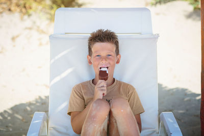 Handsome boy sitting on the beach and eating ice cream