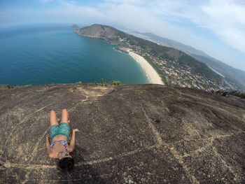 Fish-eye view of woman lying on rock formation against sky