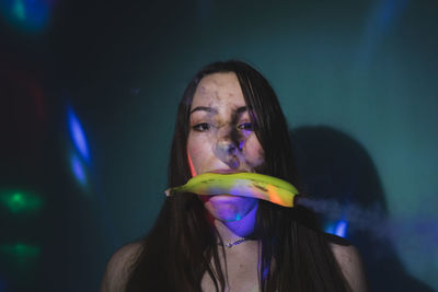 Portrait of young woman holding kiwi mouth against wall