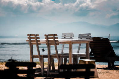 Empty chairs and tables on beach against sky