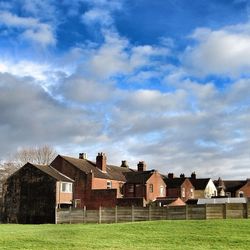 Houses on grassy field against cloudy sky