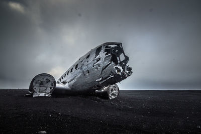 Abandoned airplane on sand at beach against sky