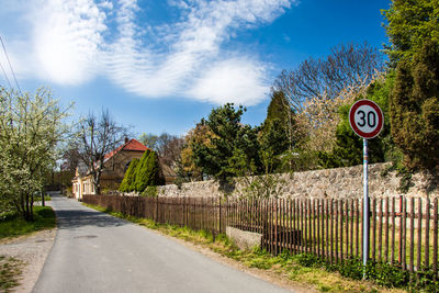 Road sign by trees against sky