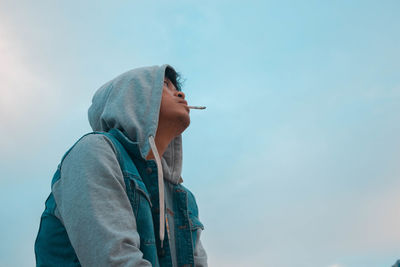 Low angle view of man smoking cigarette against sky