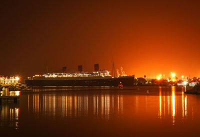 Illuminated city by sea against sky at night