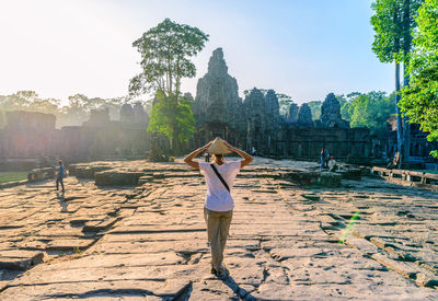 Rear view of woman wearing asian style conical hat standing on rocks during sunny day