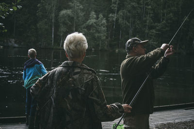 People fishing while standing at pier by lake