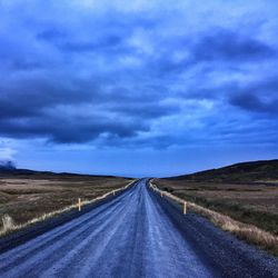 Country road amidst field against cloudy sky