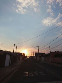 Road by buildings against sky during sunset