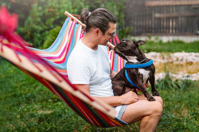 Man with french bulldog dog in hammock in the backyard during summer