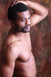 Shirtless man standing against wall