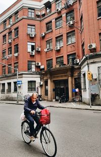 Man riding bicycle on street against buildings in city