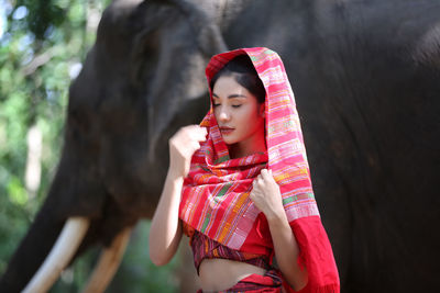 Young woman wearing headscarf while standing by elephant