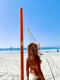 Rear view of woman sitting on beach against clear blue sky