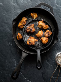 Cast iron fry pans containing deep fried fritters sprinkled with icing sugar.