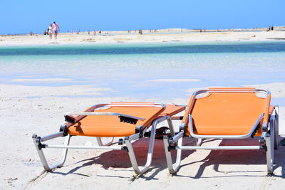 Deck chairs on beach against sky