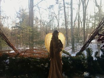 Woman standing by tree in forest against sky