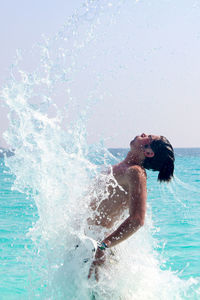 Side view of shirtless man emerging from sea against sky