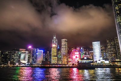 Illuminated buildings by river against sky at night