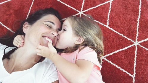 Directly above shot of cute girl kissing mother while lying on carpet