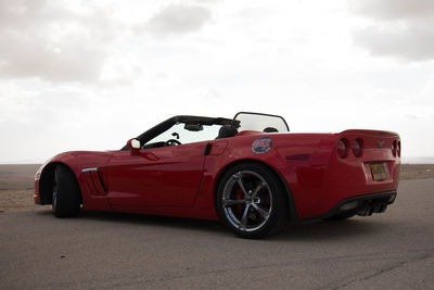 Side view of red car against cloudy sky