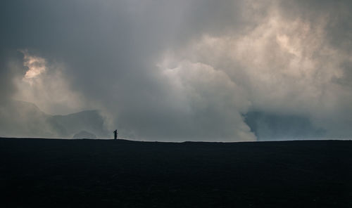 Silhouette man on field against storm clouds