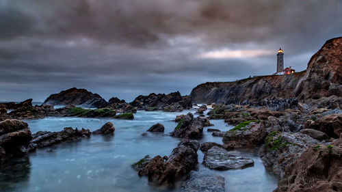 Lighthouse amidst rocks on sea against sky