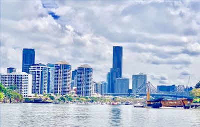 Modern buildings by river against sky in city