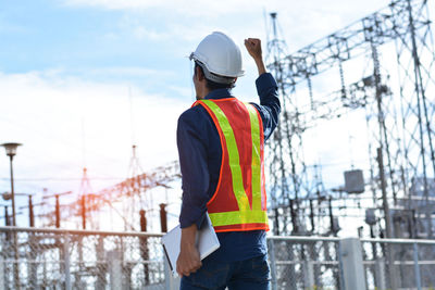 Rear view of man standing by railing against sky