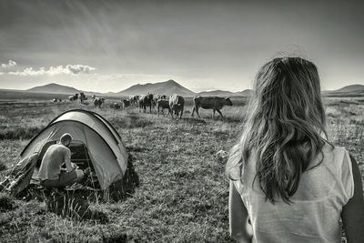 Rear view of woman with man crouching by tent on field against sky