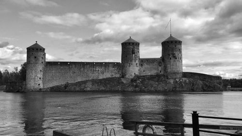 Old building by river against cloudy sky