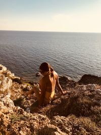 Woman sitting on rock looking at sea against sky