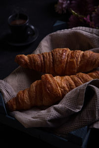 Croissants with a cup of coffee and flowers behind, on a table and dark background.