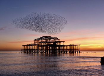 Silhouette built structure on beach against sky during sunset