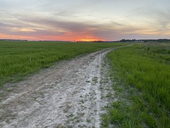 Road amidst field against sky during sunset