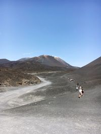 People riding motorcycle on desert against clear blue sky