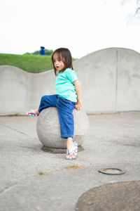 Full length of girl sitting on rock against clear sky