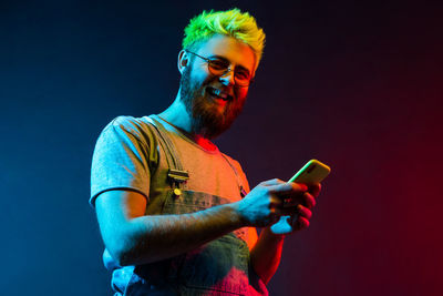 Portrait of smiling man using mobile phone against colored background