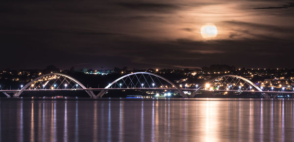 Illuminated bridge over sea against sky at night