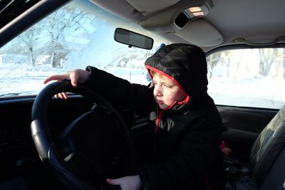 Curious boy holding steering wheel in car