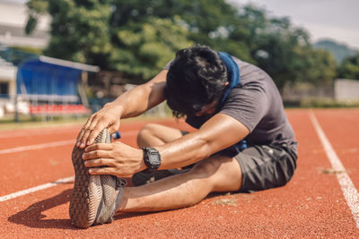 Full length of man exercising while sitting on sports track