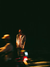 Blurred motion of man standing on illuminated road at night