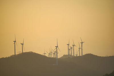 Silhouette wind turbines on hill against sky during sunset