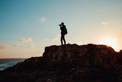 Man standing on cliff by sea against sky during sunset