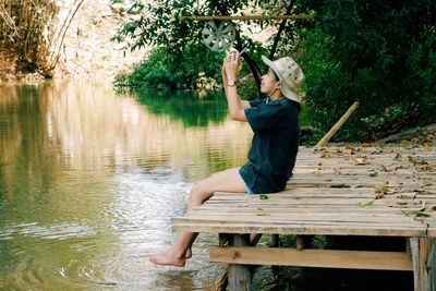 Woman sitting on wood by lake against trees