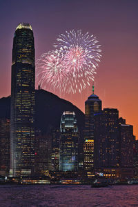 Firework display over illuminated buildings against sky at night