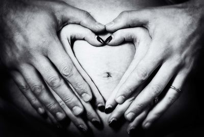 Close-up of hands making heart shape on pregnant belly