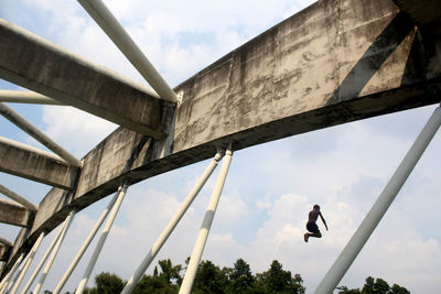 Low angle view of boy jumping from bridge against sky